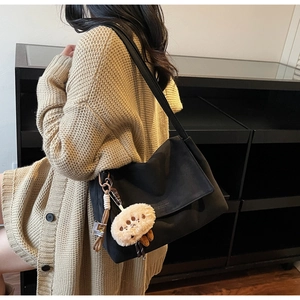 Detail of black suede tote bag with cute beige plush monster charm and wide strap