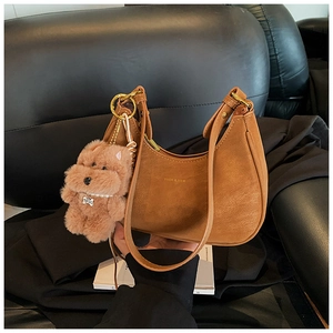 Close-up of dark brown leather crescent bag with gold logo and plush dog charm detail