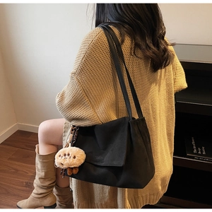 Detail of black suede tote bag with cartoon charm shown from a side angle over the shoulder