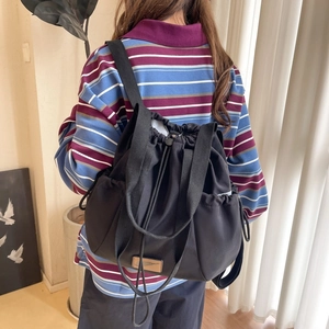 Detail view of black drawstring backpack showing nylon texture and side pockets on model