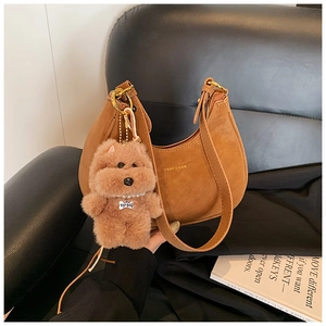 Detail of brown suede crescent hobo bag with a cute plush dog charm on a leather chair