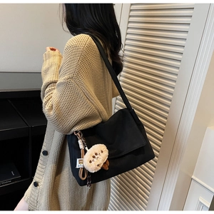 Close-up of black shoulder bag with a cute beige mushroom plush pendant and wide strap