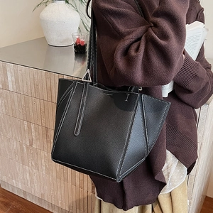 Macro shot of black pebbled leather tote bag with white stitching detail on a stone surface