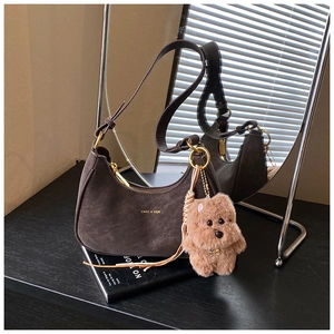 Detail of a dark brown suede hobo bag with gold logo and plush dog charm in sunlight