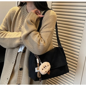 Detail of a black shoulder bag featuring a cute plush paw pendant and woven rope accents