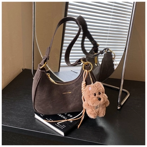 Detail of dark brown suede hobo bag with gold zipper and plush bear charm on books