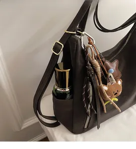 Close-up of brown matte shoulder bag side pocket with a cute bear charm and metal zipper