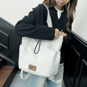 Detail view of cream drawstring tote bag with brown leather logo patch and nylon fabric