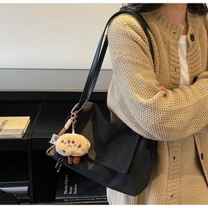 Detail of a black large capacity shoulder bag with a cute beige plush charm detail