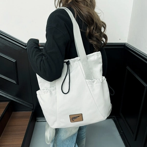 Detail of white drawstring canvas tote bag showing side pocket and leather logo patch