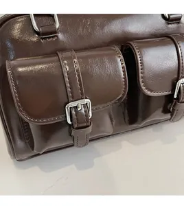 Detail of glossy oil wax leather texture and silver buckle hardware on a brown handbag