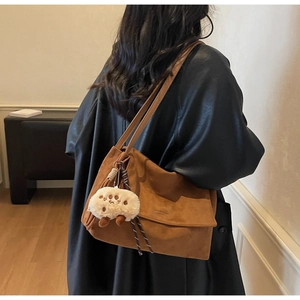 Detail of brown suede shoulder bag with a cute white plush paw charm hanging on the side