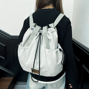 Detail of light grey multipurpose drawstring backpack featuring brown leather logo patch