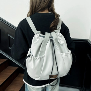 Detail of light grey drawstring backpack featuring durable fabric and brown logo patch