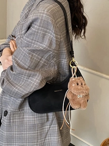 Fashionable black crescent shoulder bag with golden logo and plush puppy charm detail