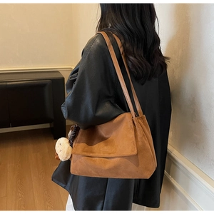Brown suede tote bag with plush bear charm worn by a model in a minimalist room
