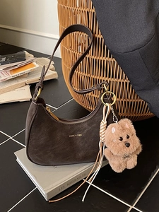 Deep brown crescent shoulder bag with leather texture and plush charm in a vintage setting