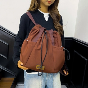 Detail of dark brown nylon drawstring backpack with side pockets and leather brand logo
