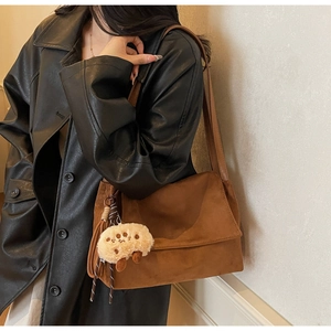 Detail view of brown suede shoulder bag featuring tassel and cute sheep plush charm