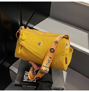 Macro detail of vibrant yellow nylon crossbody bag with textured fabric and wide jacquard strap