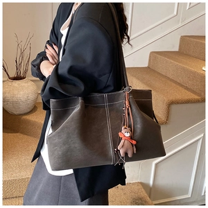 Detail view of suede tote bag with contrast stitching and small teddy bear charm