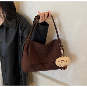 Close-up of deep brown suede tote bag with leather strap and cute plush charm detail