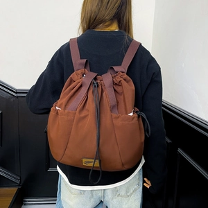 Rear view of model wearing a brown drawstring backpack with side pockets and top handles