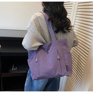 Detail view of purple nylon tote bag with functional side pockets and woven brand tag