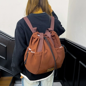 Close-up of the dark brown drawstring backpack showing the nylon texture and side pocket