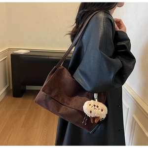 Detail of dark brown suede tote bag featuring a flip-top closure and plush charm accessory