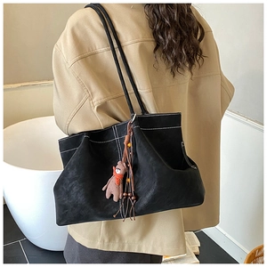 Close-up of black suede tote bag with contrast stitching and cute teddy bear charm