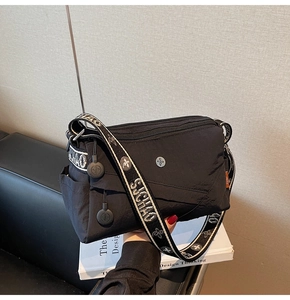 Detail view of water-resistant black nylon crossbody bag with multi-zipper layers and wide strap