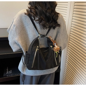 Détail du sac à dos noir mat avec pendentif ours porté par un mannequin dans une pièce