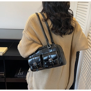 Close-up of black leather Boston bag with twin buckled pockets worn by a model