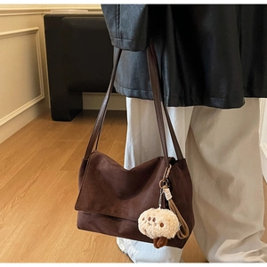 Detail of dark brown suede shoulder bag with a cute plush charm and flap closure
