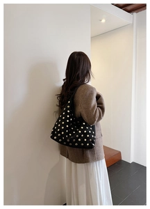 Detail of a large black suede hobo bag with gold metal studs shown on a model