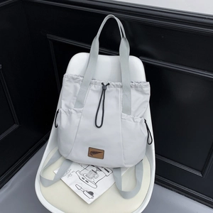 Detail view of light grey nylon backpack with drawstring closure and brown leather logo patch