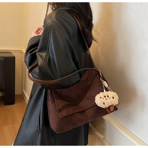 Detail view of deep brown faux suede tote bag with a plush charm on a black leather jacket