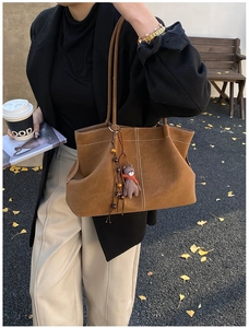 Detailed view of brown suede tote bag with white stitching and cute bear charm accessory