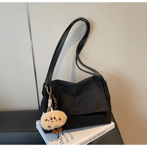 Detail of black suede tote bag with thin leather straps and a brown plush bear charm