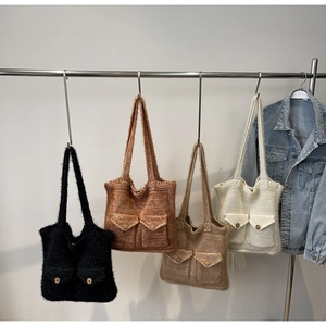 Row of chunky knit tote bags in four colors with buttoned pockets on a metal rack