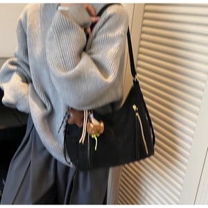 Detail of black canvas tote bag with dual front zippers and brown bear charm on strap