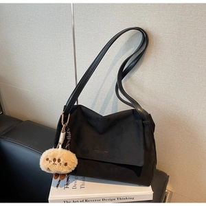 Close-up of black suede shoulder bag with a brown plush charm on a book