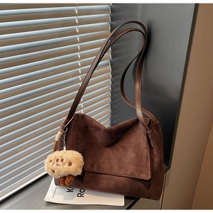 Close-up of brown suede tote bag with flap closure and cute plush toy charm on window sill