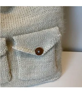 Detailed close-up of beige knitted tote bag with textured flap pocket and brown button