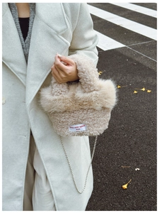 Detail of fuzzy beige plush bag with red embroidered slogan and elegant chain strap