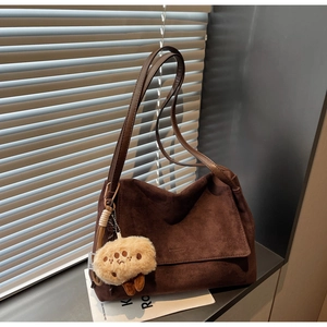 Close-up of deep brown suede tote bag with long straps and cute teddy bear charm