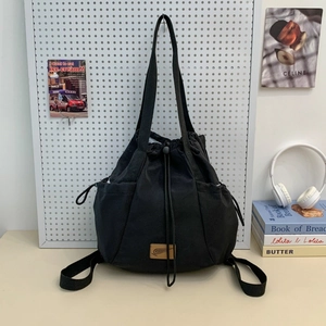 Detail of black drawstring backpack with side pockets and a brown leather logo label