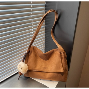 Close-up of brown suede shoulder bag featuring embossed text and a plush charm detail