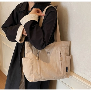 Detail of beige nylon tote bag with vertical zip pockets and wide woven shoulder strap
